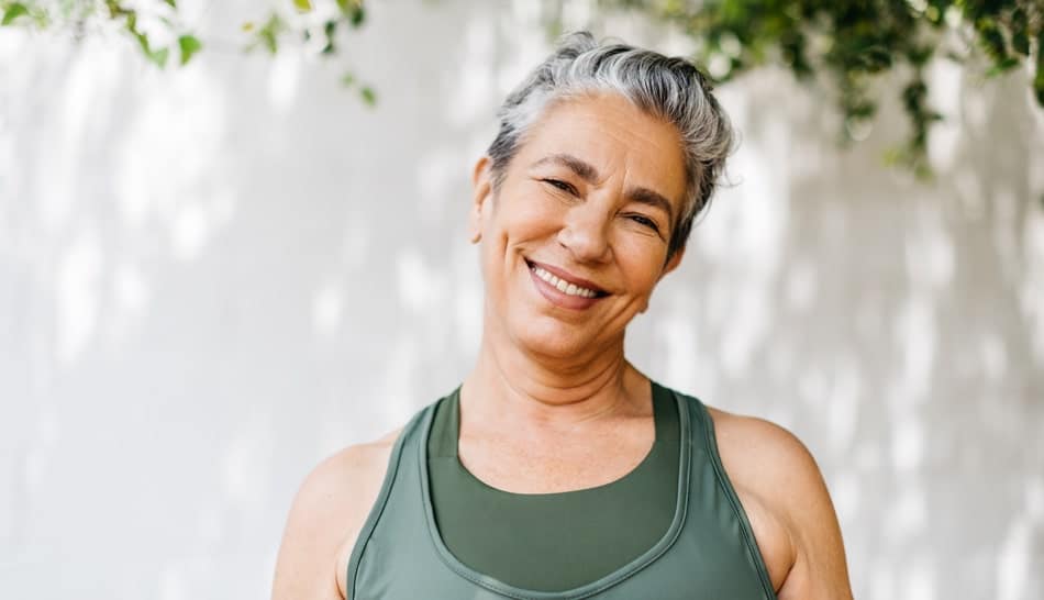 FMR content image 1 A middle-aged woman with short, gray hair standing outside in a green tank top smiling